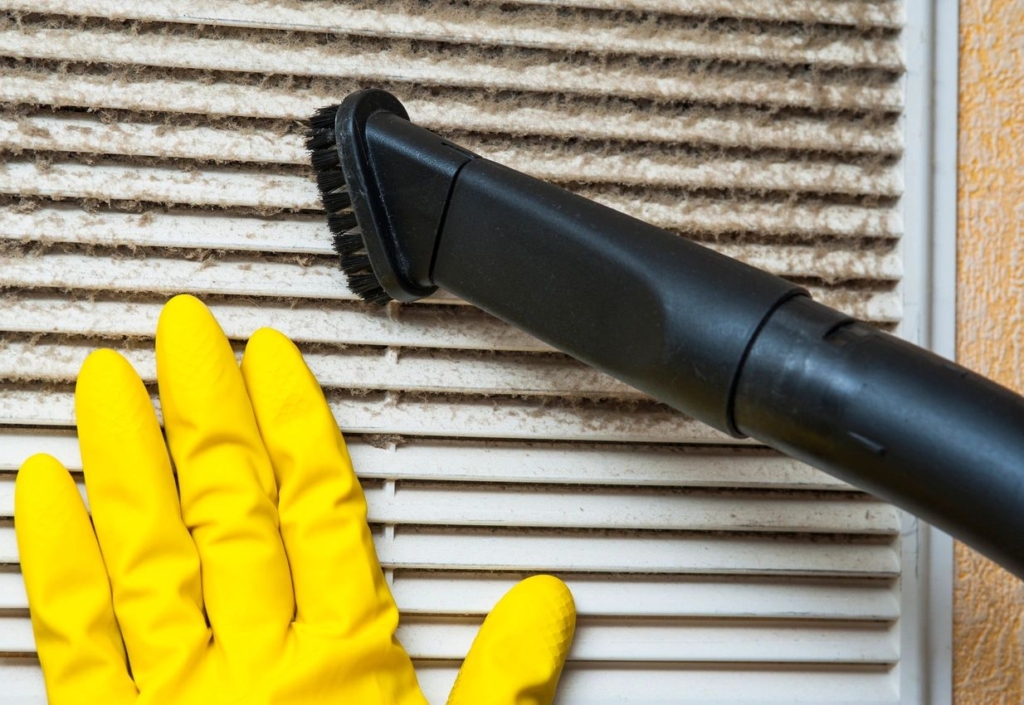 Gloved hand cleaning a vent with a vacuum